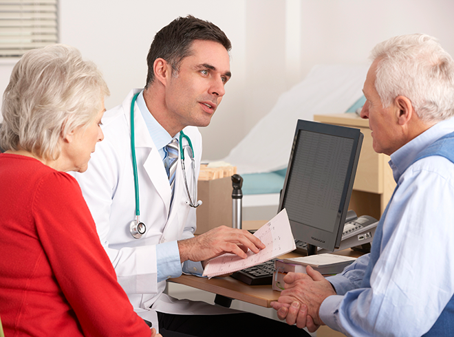 Physician discussing care plan with senior couple during office visit, highlighting shared decision-making and chronic care coordination for aging patients
