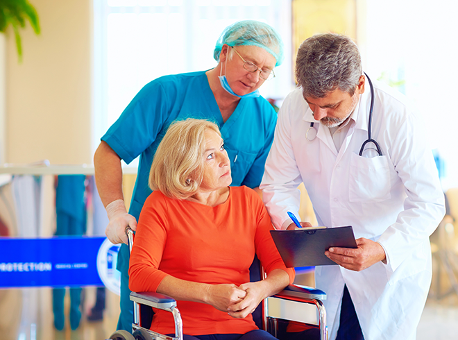 Doctor and nurse consulting with elderly female patient in wheelchair, emphasizing transitional care planning and hospital discharge coordination for senior patients